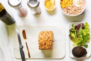 Preparing healthy sandwiches; super grains sliced bread, tuna, corn, avocado, lemon and vegetables on marble cutting board. Top view