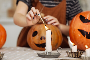 child girl lights a candle for Halloween. little girl in witch costume with carving pumpkin with a...