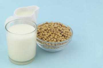 Soy milk in jug and glass with soy beans on blue background, copy space for text