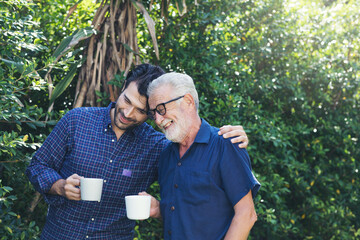 Senior father and adult son walking and talking and drinking coffee together in the garden with...