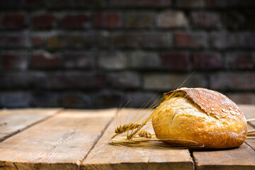 Bakery background. Whole loaf of fresh crispy bread on a wooden table with ears of wheat