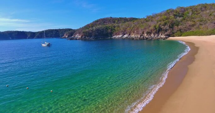 Stationary Low Angle View of Calm Water Beach Cove with Distant Anchored Sailboat