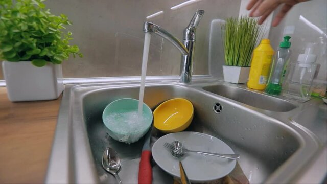 Routine in the kitchen. Dirty dishes in the sink. Tap water pours onto dirty dishes. Dishwashing process. Homework