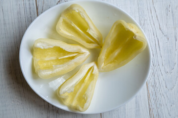 Cut in half yellow bell peppers on a white plate on a light wooden background.
