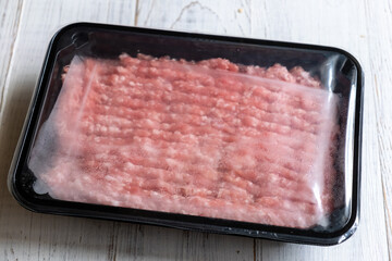 Minced meat in plastic packaging on a light wooden background.