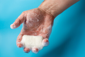 Global Handwashing Day, personal hygiene concept. A man's hand in foam holds soap on a blue background.