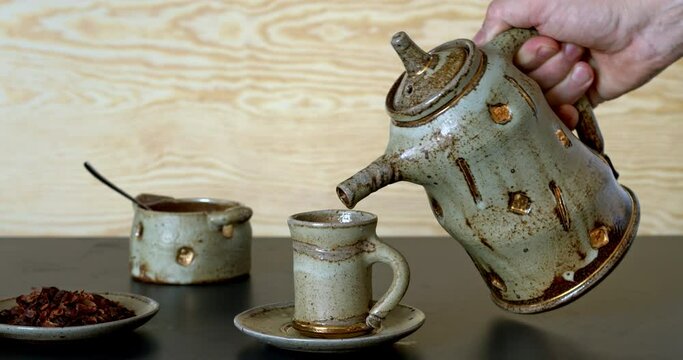 Pouring cascara beverage in unique ceramic teapot to tea cup.