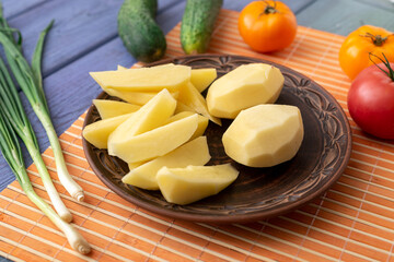 Tubers of raw peeled cut potatoes on a plate on the kitchen table with vegetables. Preparation for cooking.