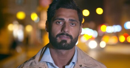 Bokeh shot of handsome indian man looking at camera in city at night