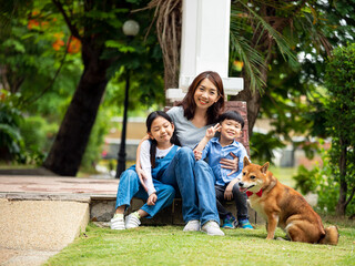 Fototapeta premium Asian mother and kids sitting and playing together with Shiba inu dog in public park