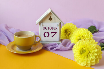 Calendar for October 7 : decorative house with the name of the month in English with the numbers 07, a bouquet of yellow dahlias on a light pastel scarf, side view, multi-colored background