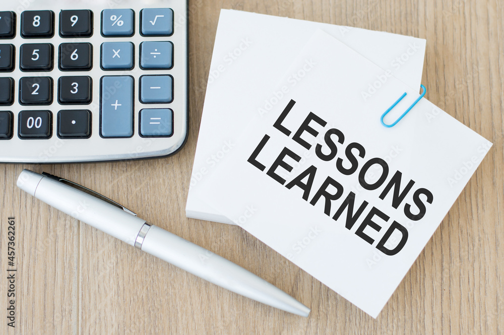 Poster text lessons learned on white note paper on the table next to a calculator and a pen. financial conc
