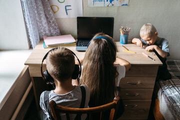 Group of schoolkids or friends wearing headphones sitting near laptop at home. Family, school pupil distance learning, online virtual class on laptop by video conference call, watching tv lesson.
