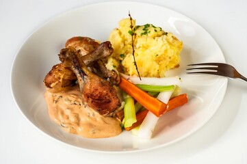 Baked chicken thig, mashed potato, olive mayonnaise and vegetable on white plate.