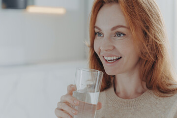 Ginger woman drinks pure water from glass enjoys refreshing drink