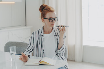 Woman sits at table makes notes in notepad uses virtual assistant to record message or make call