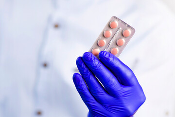 Doctor in gloves holds pills. Guy with protective gloves. Pink pills in hands. The guy holds out the pills. Treatment methods. Disease prevention. Health care.