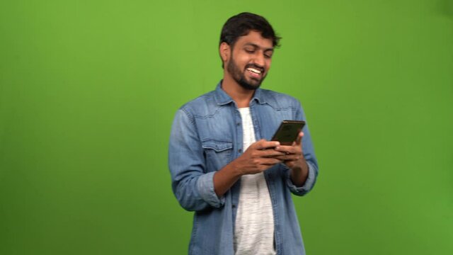 Young Asian netizen happily texting with someone on mobile phone; green screen shoot.