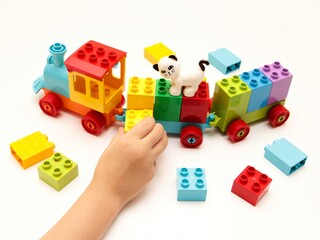 child builds a train constructor from plastic building blocks on a white background.  children is educational games