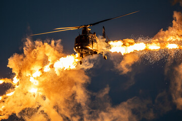 Legerhelikopter die tijdens de vlucht defensieve flare-lokvogels afvuurt in de schemering.