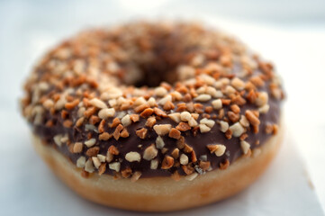 A chocolate donut with hazelnut sprinkles lies on a white surface. Fried dough confection, dessert food, sweet snack with chocolate glazing and nut crumbs. Delicious fresh donuts concept.