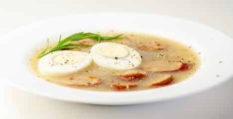 Traditional polish sour soup with sausage and eggs in a white deep plate