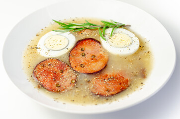 Traditional polish sour soup with sausage and eggs in a white deep plate