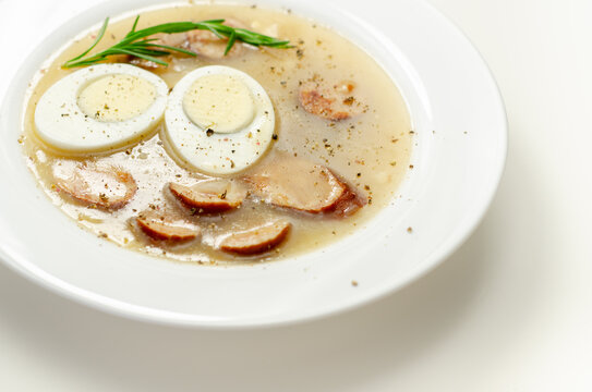 Traditional polish sour soup with sausage and eggs in a white deep plate