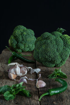 Still life with green broccoli, chiles, garlic and mint on wood board