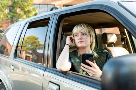 Teen Looking Out Passenger Window Of Car Holding Cel Phone Downtown