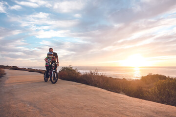 Father helping son ride his bike on a coastal trail at sunset.