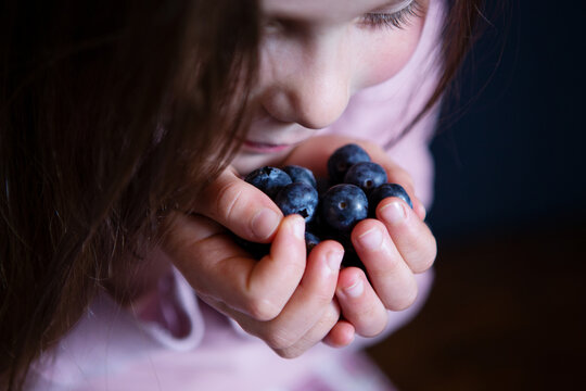 Smiling girl picking fresh blueberries on dark background