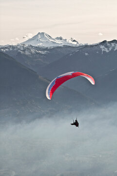 Silhouetted Paraglider sails through the air near Mount Baker.
