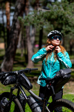A woman next to her mountain bike fastening her protective helmet