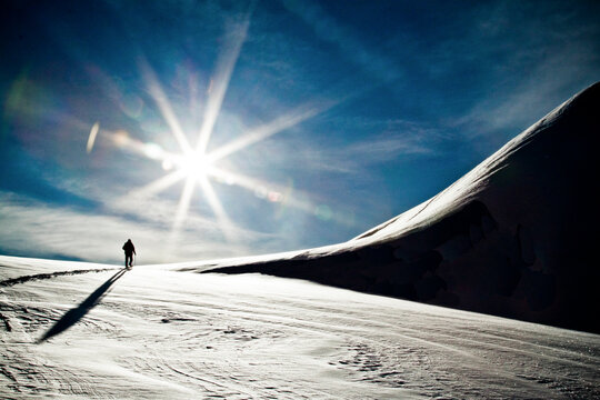 Rear view of silhouetted person ski touring towards snowy mountain.