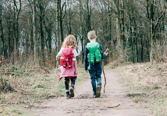 two kids hiking together with sticks and backpacks talking in the UK