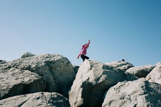 young girl running along large rocks playing in the sunshine