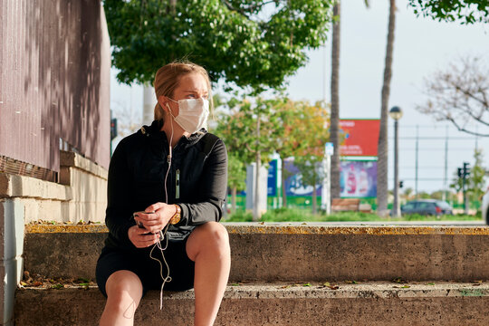 Woman in sportswear and face mask looks at her phone sitting on stairs