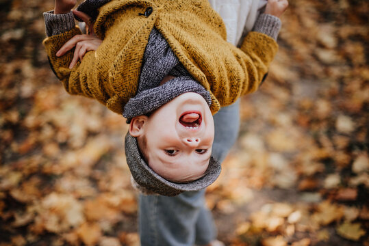 Stylish boy having fun in autumn city park. Happy kid walking among fallen leaves. Kids fashion. Boy wearing trendy yellow coat, cap and scarf. Smiling young boy outdoors. Kid jumping and run