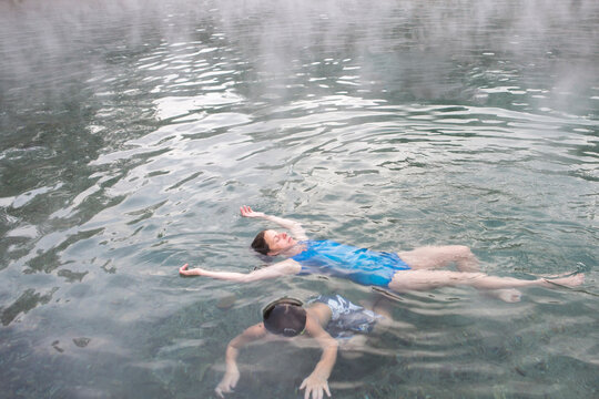 A mother and son float in Trinity Hot Springs pool with steam rising