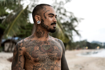 Thai guy on the seashore among the palm trees all in tattoos