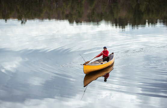 Teen boy paddling a canoe alone on a calm lake in Canada.