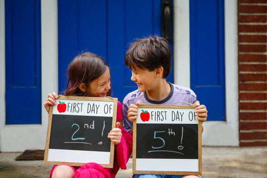 Two happy children sit together on stoop holding Back-to-School signs