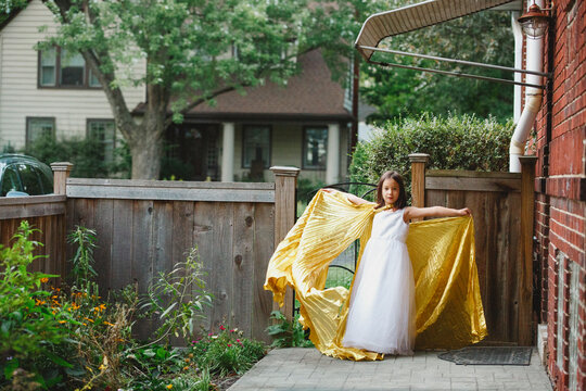 A little girl stands in garden arms outstretched in long gold cape