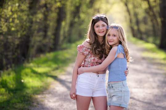 Two pretty teen girls, best friends, standing on tree lined road.
