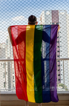 Gay man holding the rainbow flag symbol of gay pride on a balcon