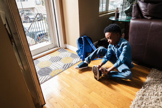 Boy wearing shoe while sitting by entrance of home
