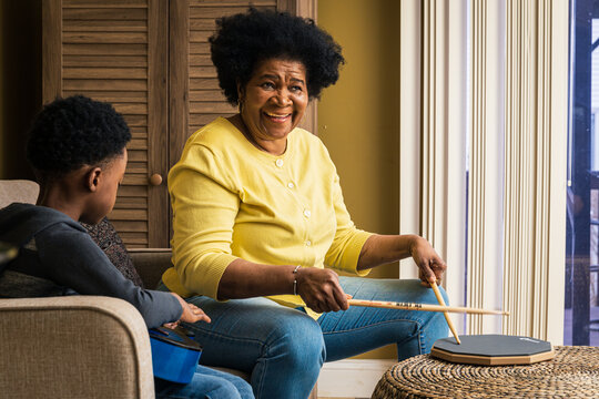 Cheerful senior woman playing drum pad while grandson practicing guitar at home