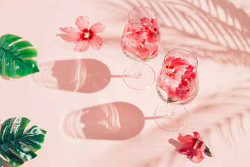 Summer creative composition made of two glasses with hibiscus flower water on pastel pink background with palm tree leaf shadows and monstera leaves.  Refreshment concept