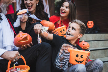 excited boy holding lollipops near family in halloween costumes